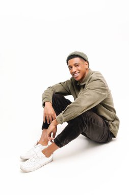 Şapkalı mutlu Afro-Amerikalı adamın dikey fotoğrafı. Rahat poz vermiş, beyaz arka planda izole edilmiş. Çekici gülüşü olan ve kameraya bakan olumlu bir adam.