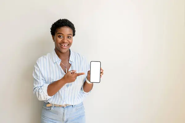 Happy African-American woman point fingers at empty smartphone screen, advertising new mobile app multiracial female office employee looking at the camera, copy-space, isolated on white, template