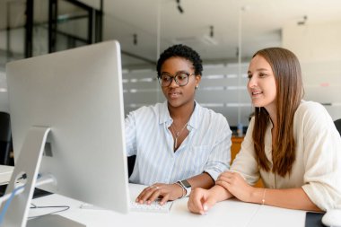 Modern açık uzay ofisinde yan yana oturup bilgisayar monitörüne bakıp gülümseyerek dostane çalışma ortamının keyfini çıkarmayı tartışan iki bayan meslektaşım.