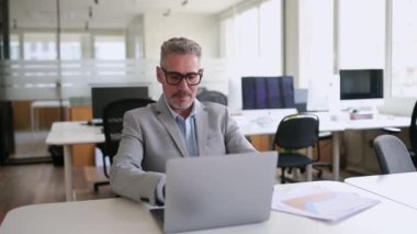 Konsantre olmuş, 50 'li yaşlarda, iş kıyafetleri içinde gri saçlı bir ofis çalışanı, masada oturuyor, dizüstü bilgisayarda yazıyor, iş adamı proje üzerinde çalışıyor, müşteriye e-posta yazıyor.
