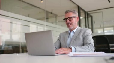 Yakışıklı, gri saçlı iş adamı video görüşmesi yapıyor, el sallıyor, bilgisayarla sanal konferans yapıyor, görüşmelere öncülük ediyor, çevrimiçi toplantı sırasında iş arkadaşlarını selamlıyor.