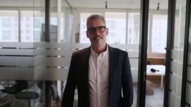 Dertsiz tasasız, olgun bir erkek çalışanın modern ofis alanında yürümesine ilham kaynağı oldu. Resmi ceketli 60 'lı yılların iş adamı hafif bir gülümsemeyle kameraya baktı.