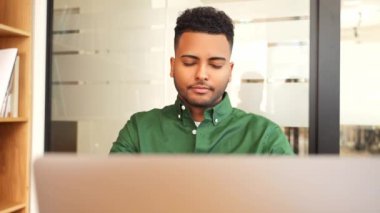 Çalışmak için dizüstü bilgisayar kullanan bitkin Hintli bir adam. Sıradan giyinen erkek çalışanın alnına dokunup masaj yapması, yorgun ve bitkin hissetmesi, ofiste gözleri kapalı oturması...