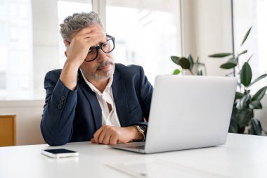İçerde dizüstü bilgisayar kullanan düşünceli bir erkek ofis çalışanı, kafası karışık bir yüz ifadesi olan dizüstü bilgisayara bakıyor, iş adamı çözme görevleri, finansla ilgili sorunlar yaşıyor.