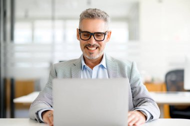 Resmi kıyafetleri ve gözlükleri olan, masada oturan, iyi modda bir erkek çalışan olan olgun iş adamının ön görüntüsü.