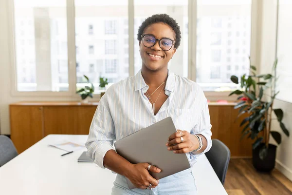 成功したアフリカ系アメリカ人のビジネスマンの肖像画 立ってオフィスでラップトップを運ぶ カメラを見て ギャップで微笑んで 陽気な女性起業家 フリーランサーや学生 — ストック写真