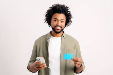 İnternetten alışveriş yapmak için akıllı telefon ve kredi kartı kullanan neşeli bir adam. Mutlu adam internetten yemek sipariş ediyor. Erkek, uzun zamandır beklenen cep telefonunun parasını ödüyor.