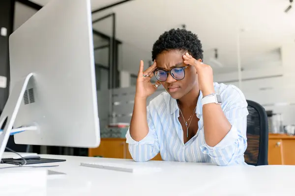 Frustrated african-american businesswoman worrying about project, sitting at the desk in front of PC, depressed female employee feeling stress by mistake or unexpected computer error crash, headache