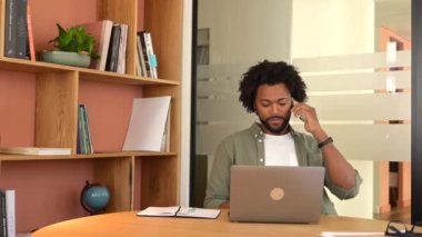 Arkadaş canlısı gülümseyen Afro-Amerikan erkek çalışanı modern ofis yerinde oturarak keyifli bir telefon görüşmesi yapıyor, yeşil tişörtlü neşeli iş adamı akıllı telefondan konuşuyor.