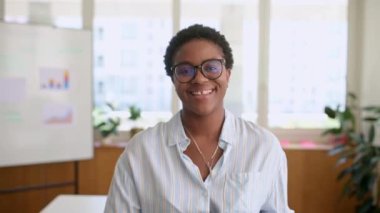 Gözlüklü başarılı Afro-Amerikan iş kadını portresi ayakta duran ve ofiste dizüstü bilgisayarını taşıyan, kameraya bakan ve aralıklı, neşeli bayan girişimci, serbest çalışan veya öğrenci ile gülümseyen