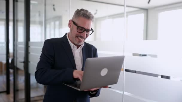 優雅な灰色の髪の成熟した50代のビジネスマンは 屋内ラップトップを使用してスマートなカジュアルジャケットを身に着けています 男性のオフィスの従業員のビジネスオーナーは コンピュータを保持し メッセージを入力 彼の仕事を楽しんで — ストック動画