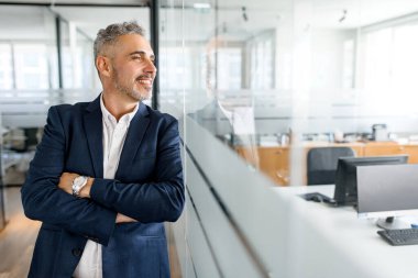 Modern ortak çalışma alanında çalışan, kollarını kavuşturmuş, resmi kıyafetli olgun bir iş adamı, erkek serbest çalışan ya da çalışanı neşeli bir şekilde başka tarafa bakıyor, yeni bir projeye başlamaya hazır.