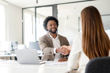 Çağdaş ofis ortamında bir erkekle bir kadın arasındaki sıcak tokalaşma, iş dünyasında dostça bir anlaşmayı ya da selamlaşmayı simgeler.