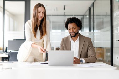 Bir kadın, profesyonel bir bağlamda etkileşimli iletişim ve takım çalışmasını gösteren içeriği erkek bir meslektaşla tartışırken bir dizüstü bilgisayar ekranına işaret ediyor..