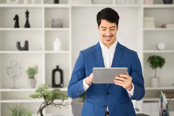A cheerful Hispanic businessman interacts with a tablet, with a look of satisfaction, in a well-organized office, concept of digital tools for business efficiency