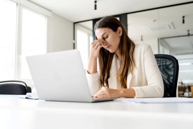 Endişeli bir iş kadını laptopuyla uğraşırken burnunun köprüsünü çimdikliyor. Kadın bir ofis çalışanı işyeri stresi ya da karmaşık bir sorun üzerine derin düşüncelere dalmış.