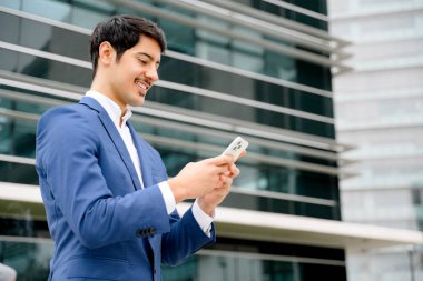 İspanyol girişimci mutlu bir şekilde akıllı telefonunu kullanıyor, etrafındaki açık alan modern iş hayatına esnek bir yaklaşım öneriyor. Resmi takım elbiseli neşeli adam internette mesaj atıyor.