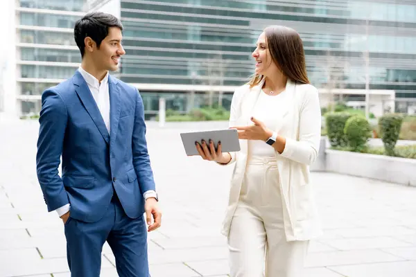 Two business partners share a laugh while discussing work on a digital tablet, embodying the harmony of professional relationship and a positive work environment.