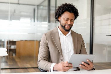 İş adamı, iş analizi veya proje yönetimi ile ilişkili dijital içerikle etkileşimde bulunan bir tablete odaklanmış durumda. Teknolojinin kullanımı, ticarete esnek ve modern bir yaklaşımı temsil eder..