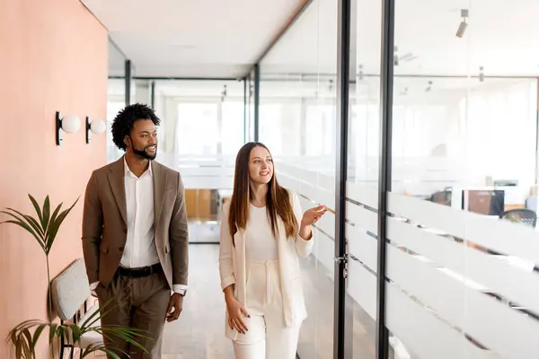 African-American businessman and his female colleague share a strategy vision walking through the office, with genuine smiles indicating a positive work culture. Concept of collaboration and teamwork