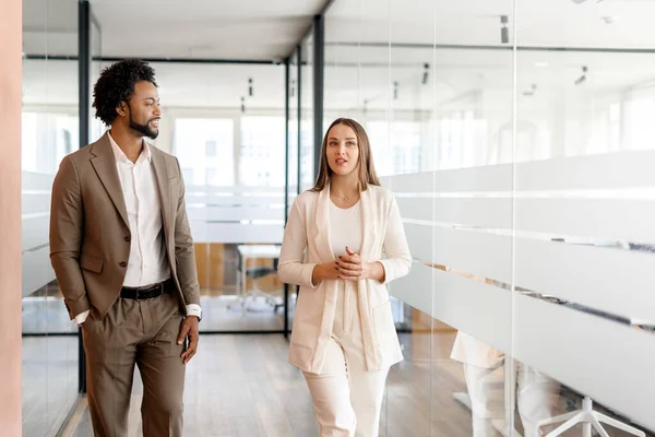 A businesswoman leads the way in an office hallway, with a male colleague alongside her, both exemplifying leadership and a forward-thinking business approach. Teamwork concept
