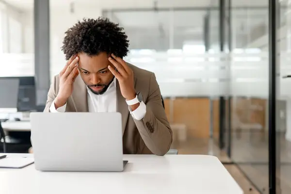 ストレスを受けたアフリカ系アメリカ人の実業家は 彼が意図的にオフィスで彼のラップトップスクリーンを研究しているという懸念の兆候を示しています 専門的な責任を伴う課題とプレッシャーの概念 — ストック写真