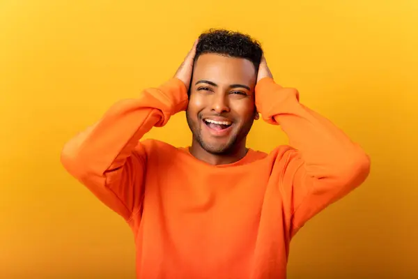 Excited shocked man holding hands on face and screaming looking at camera with open mouth, shocked bemused with news, win at lottery. Indoor studio shot isolated on yellow background