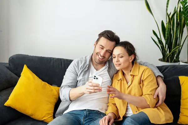 Neşeli bir çift evde akıllı bir telefonla vakit geçirir. Bir eş ve bir koca, rahat oturma odasındaki kanepede oturmuş gülümseyerek videolar izler, beslenir ve güler.