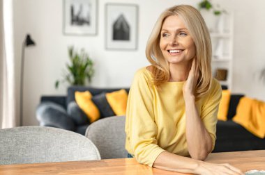 Kaygısız orta yaşlı bir kadın koltukta oturuyor ve dinleniyor. Evde hayal kuran çekici olgun bir kadının yatay görüntüsü.