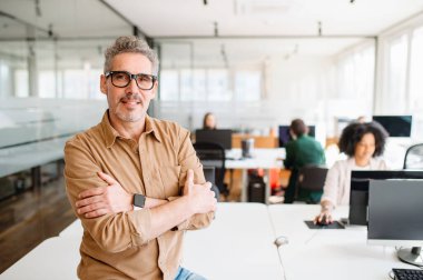 Üst düzey bir profesyonel çalışma alanını güvenle denetlemek için bir ofis masasına yaslanıyor. Onun gelişigüzel ama otoriter varlığı, hareketli bir ofis ortamında yaklaşılabilir bir liderlik tarzını işaret ediyor.