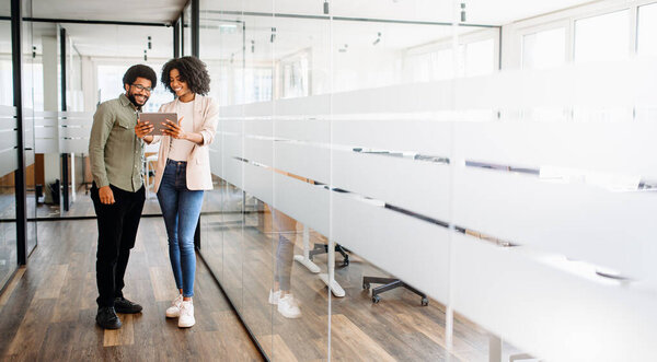 A professional duo exudes confidence and collaboration in an office, with woman showing content on a tablet to engaged male colleague, highlighting a moment of shared focus and constructive feedback