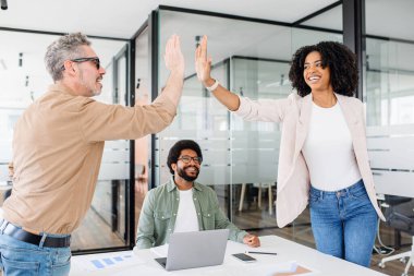 Modern ofis alanındaki meslektaşlar arasında yapılan beşlik bir jest, çevreleyen ekibin sevinçli bir çalışma ortamı olan sevinç dolu ruhu paylaştığı başarılı bir anı vurguluyor.