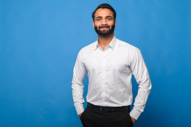 Resmi beyaz gömlekli, iyi giyimli bir Hintli elleri mavi arka planda, güvenli bir şekilde duruyor. Profesyonellik, iş ve şık günlük kıyafetler..