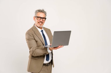 Resmi takım elbiseli, gözlüklü, dizüstü bilgisayarla kameraya bakan gri saçlı iş adamı. Bu resim çevrimiçi işletme yönetimi ve konsantre çalışma için idealdir.