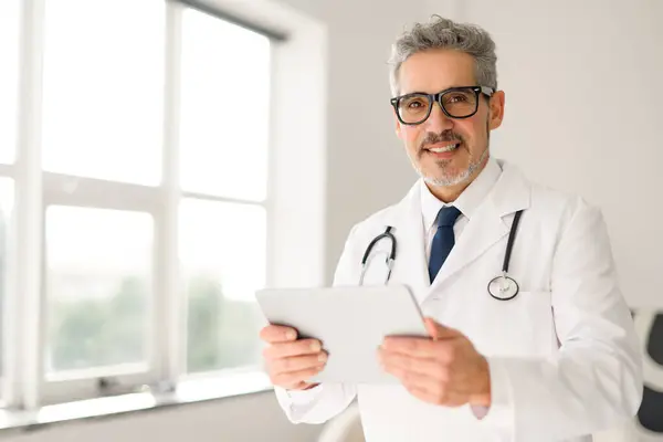 Starší Lékař Brýlemi Přátelské Chování Drží Tablet Stojí Okna Přirozeným — Stock fotografie