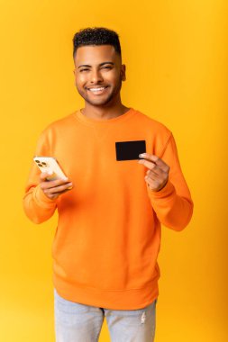 Neşeli orta doğulu adam internet üzerinden alışveriş yapmak için akıllı telefon ve kredi kartı kullanıyor. Mutlu Hintli adam internetten yemek sipariş ediyor. Uzun zamandır beklenen cep telefonunun parasını ödüyor.