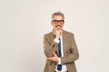 Deneyimli profesyonel düşüncelere dalmış, eli çenesinde, stratejik düşünme ya da karar verme anını somutlaştırıyor, bilgelik kavramlarını temsil ediyor, kameraya bakıyor ve gülümsüyor.