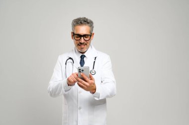 Dostane bir tavrı olan kıdemli bir doktor elinde bir akıllı telefon tutuyor, tıbbi bilgileri gözden geçiriyor ya da randevularını ayarlıyor, boynuna bir stetoskop sarılı ve konsantrasyon bakışlarıyla.
