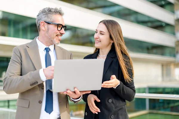 stock image A senior businessman with a grey hair shares ideas and strategy with a young female colleague over a laptop, reflecting teamwork and mentorship in a modern corporate setting