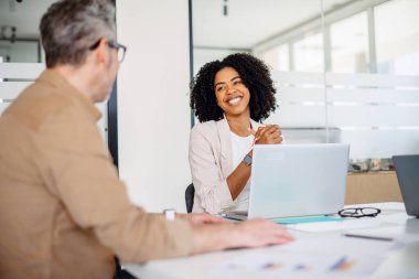 Profesyonel bir toplantı takım çalışmasının özünü yakalar, neşeli bir kadın çalışanla birlikte olgun bir erkek meslektaşla proje detaylarını tartışır, dinamik ve çekici bir çalışma ortamını yansıtır.