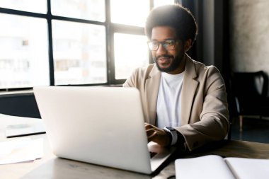 Genç bir girişimci işine bir dizüstü bilgisayarla dalmış, şık giyimi ve sıcak gülüşü hem yakınlık hem de profesyonelliği gösteriyor. Arka planda açık tavan arası pencereleri