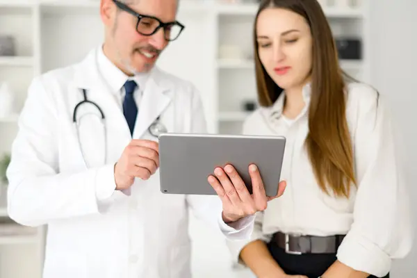 Dospělý Doktor Stýká Mladou Pacientkou Ukazuje Něco Digitálním Tabletu Který — Stock fotografie