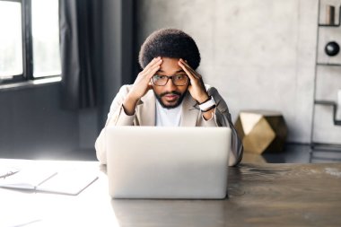 Brezilya 'daki genç bir işadamı, şirket sorumluluğunun zorlu yönlerini temsil eden dizüstü bilgisayarı üzerinde çalışırken stres belirtileri gösteriyor. El ele tutuşmaktan yorgun erkek çalışanlar.