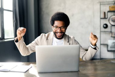 Brezilyalı işadamı, çağdaş bir ofis olan dizüstü bilgisayarında zaferini kutlarken sevinç saçıyor. Yumrukları ve gülüşü, mesleki hayatın başarı, başarı ve zevklerini anlatıyor.