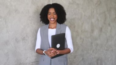 Profesyonelliği ortaya çıkaran Afro-Amerikalı bir kadın elinde dizüstü bilgisayarla, modern iş kıyafetlerini rahatlıkla harmanlayan iş kıyafeti giyer.