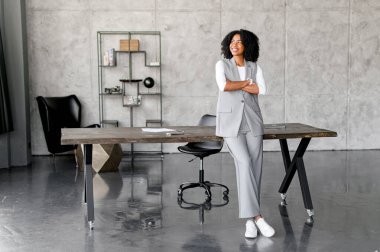 Gösterişli bir ofis masasının yanında duran bu Afro-Amerikalı iş kadını, kendine güven ve modernlik yayıyor..