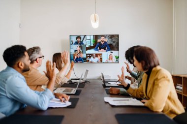 Diverse team of professionals enthusiastically participates in a video conference call, waving hands, reflecting a warm and inclusive company culture that embraces remote collaboration and team unity clipart