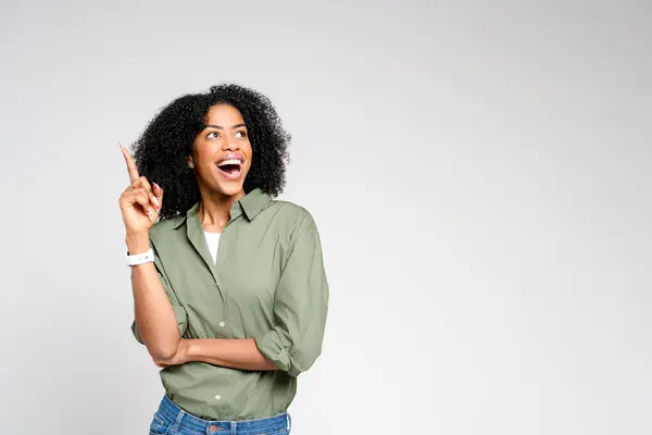 アフリカ系アメリカ人女性が喜びを放射し 彼女の顔は興奮とともに上向きを示し 明白な背景に新しいアイデアや楽しい例外を示しています — ストック写真