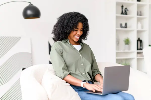 Afroamerykańska Kobieta Pochłonięta Pracą Pisze Laptopie Siedząc Kanapie Ucieleśniając Elastyczność — Zdjęcie stockowe