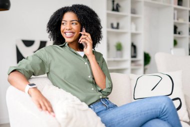 Bir telefon görüşmesinde kahkaha atarken yakalanan kadın, kıvırcık saçlarıyla zevk ve rahatlık saçıyor. Yüzüne mükemmel bir çerçeve çiziyor. Evden sevdikleriyle bağ kurmanın rahatlığını özetliyor.